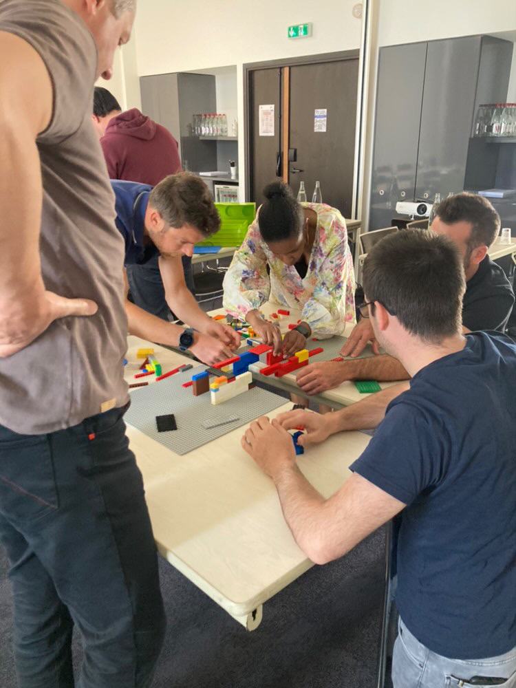 LEGO challenge Brussel deelnemers debriefing in lichte zaal met uitzicht op stad · INNOV'events